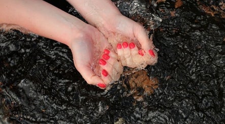 Hands with red nails under spa water at Garden Nail Haven, Chester, England, GB.