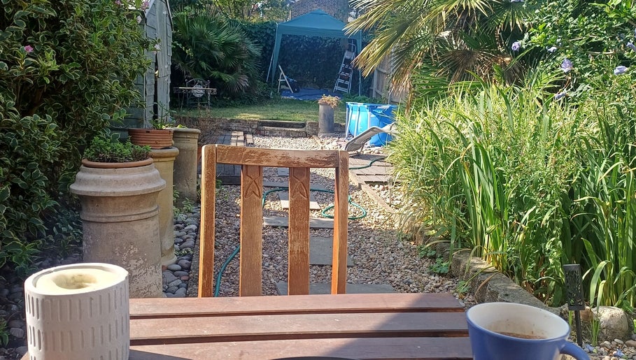 Tranquil garden view at MaxRelax Massage Therapy, London, England, GB, with a wooden chair and lush plants.