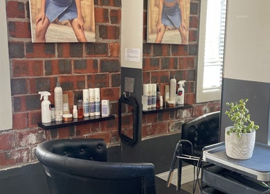 Modern salon interior at Hair by Tess, Cape Town, Western Cape, ZA with chairs, products, and brick wall.