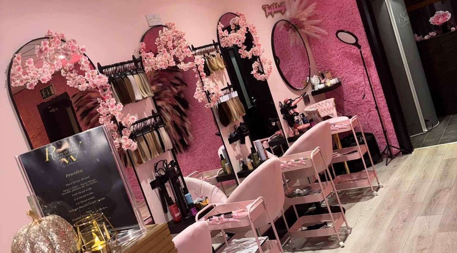 Inside Runway Hair Extensions by Sharon, Ardee. Elegant pink salon interior with mirrors and hairpieces on display.