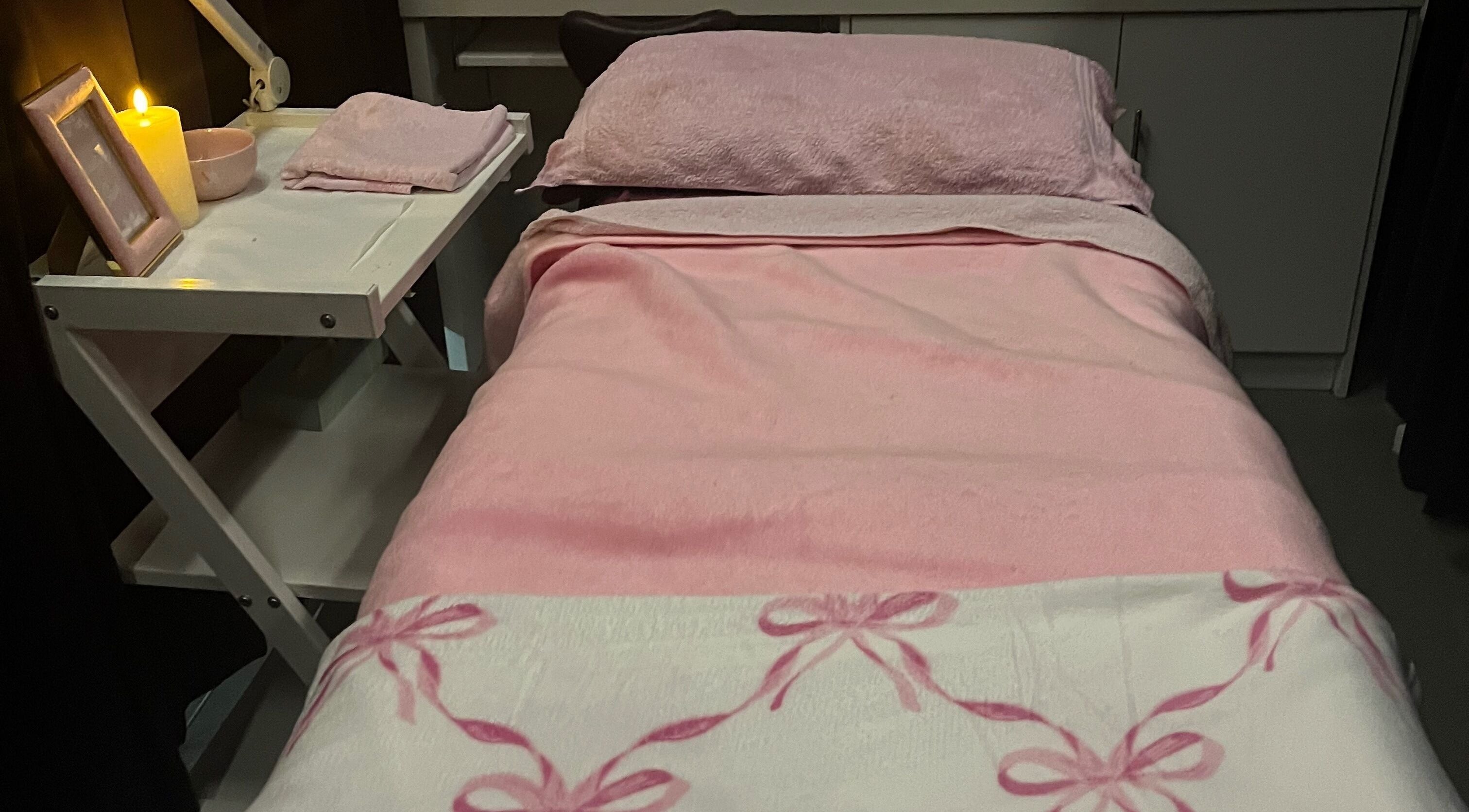 Cozy treatment bed at Beautybysxph, Hamilton, Scotland, GB, with pink linens and warm lighting.