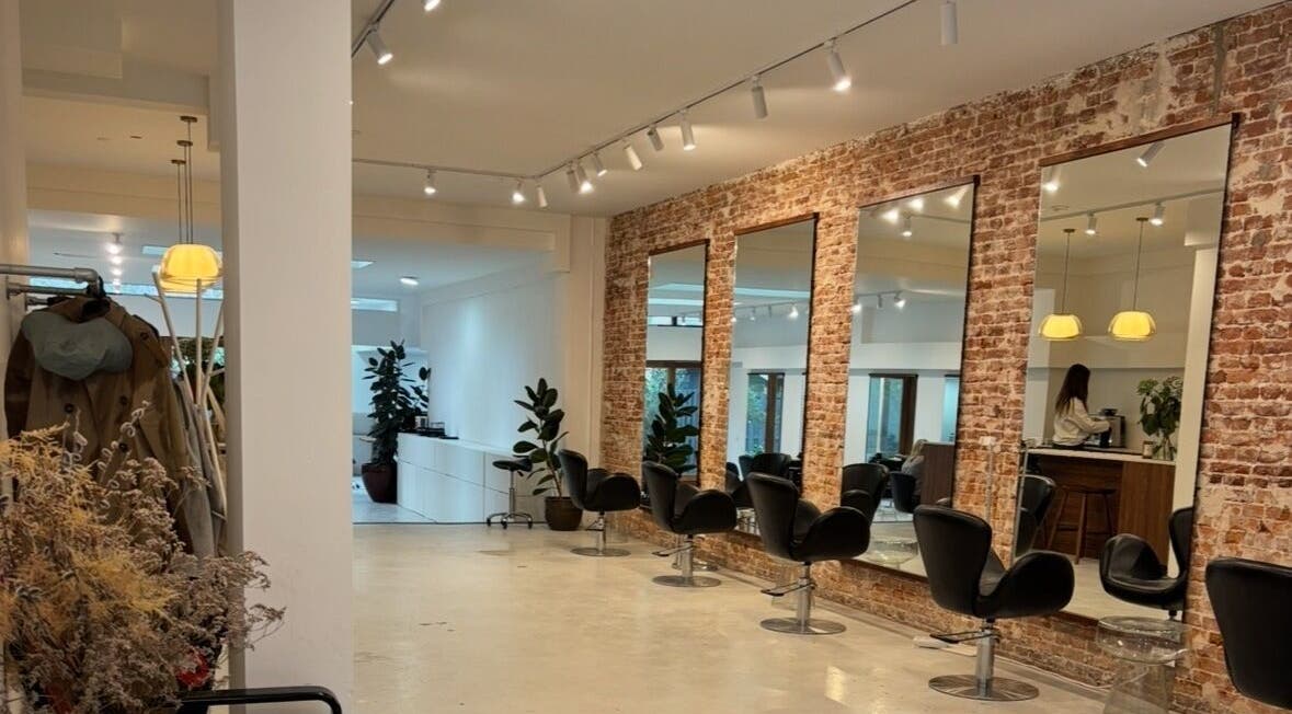 Interior of Pascale Marie Hair, Amsterdam, Noord-Holland, NL, featuring modern chairs and brick-accented walls.