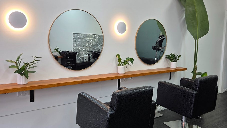 Elegant mirror setup at Papillon salon, Hendra, Queensland, AU with black chairs and lush green plants.