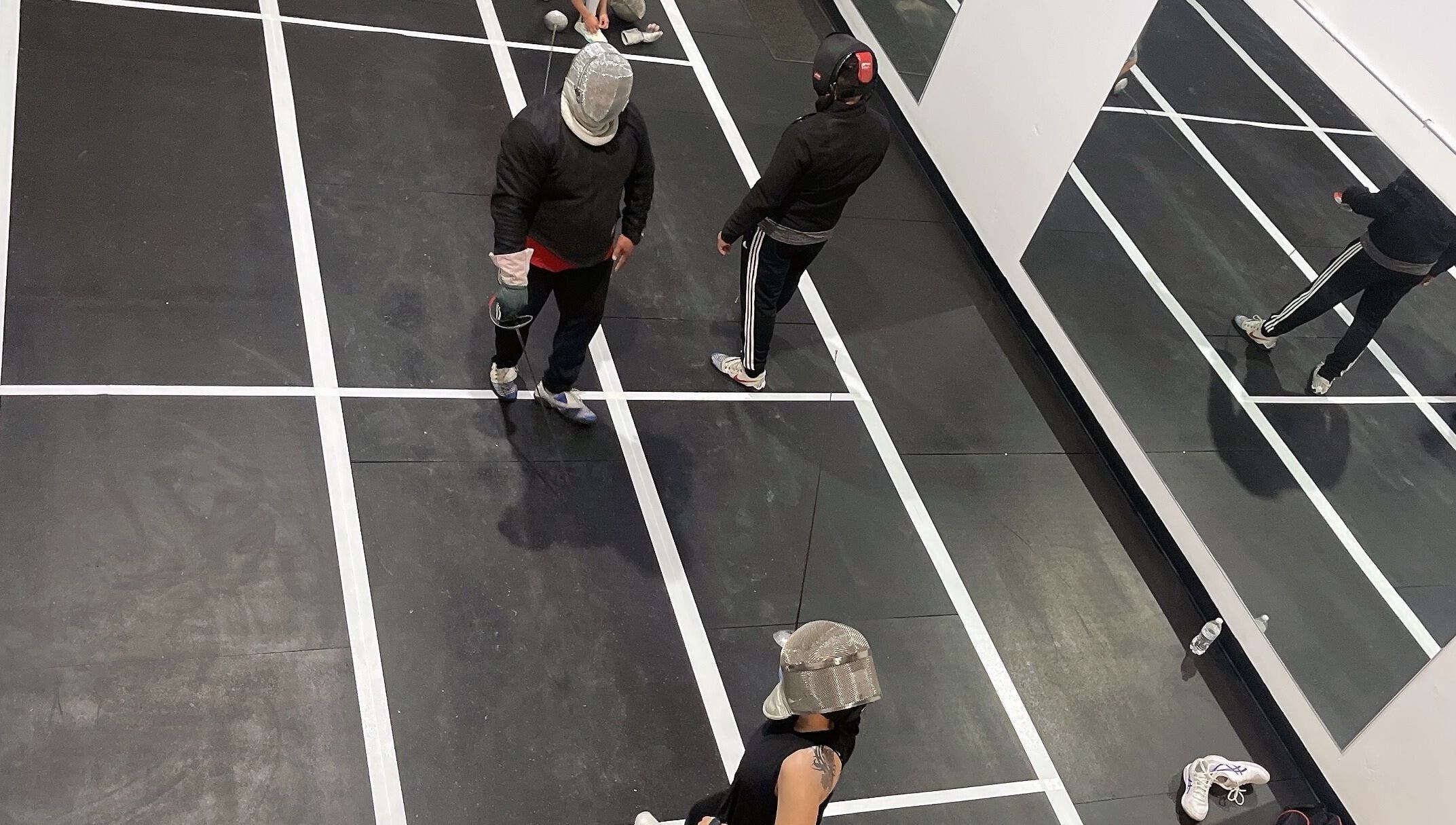 Fencers in action at Fence MI Fencing Academy, Las Vegas, Nevada, US, featuring mirrored walls and marked floors.