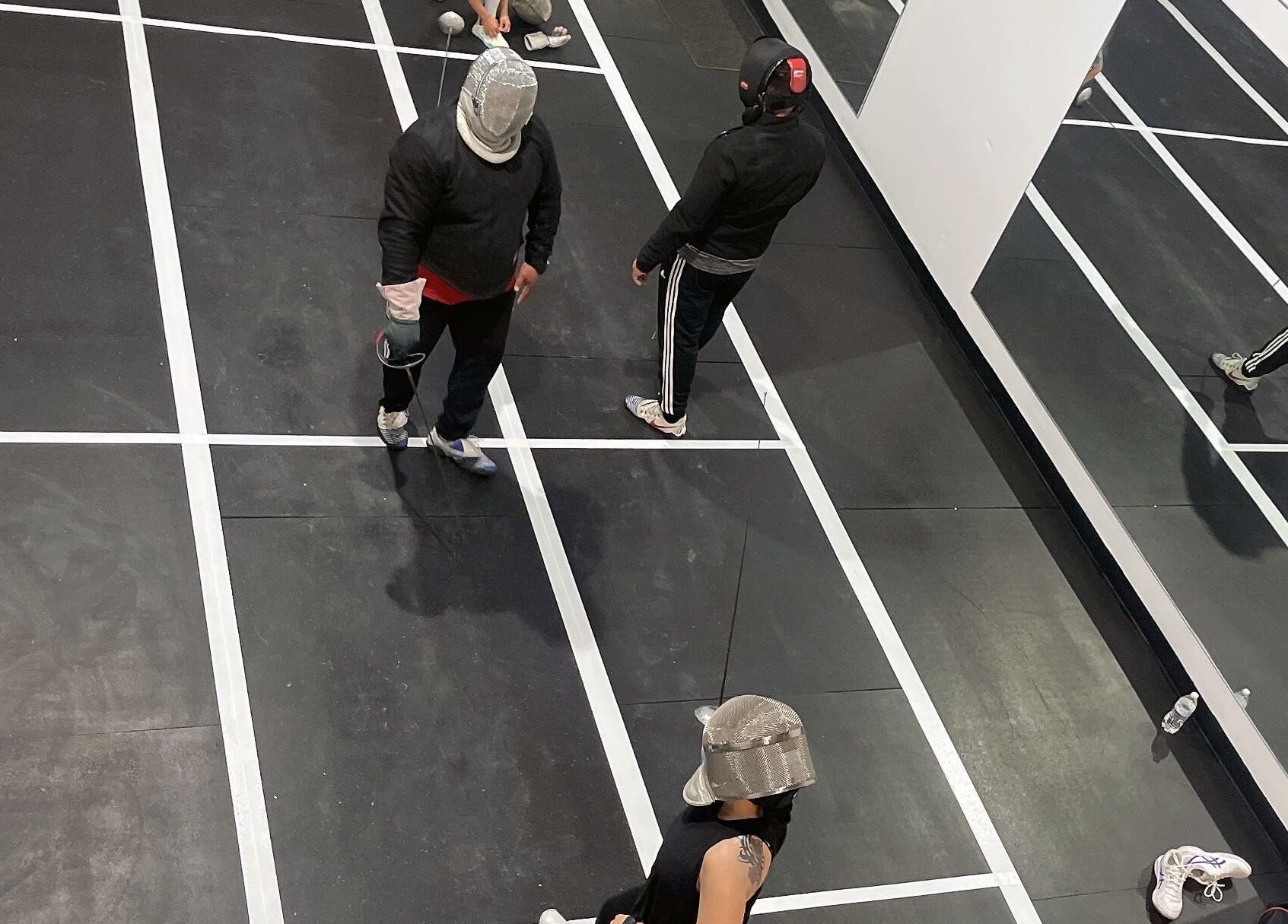 Fencers in action at Fence MI Fencing Academy, Las Vegas, Nevada, US, featuring mirrored walls and marked floors.