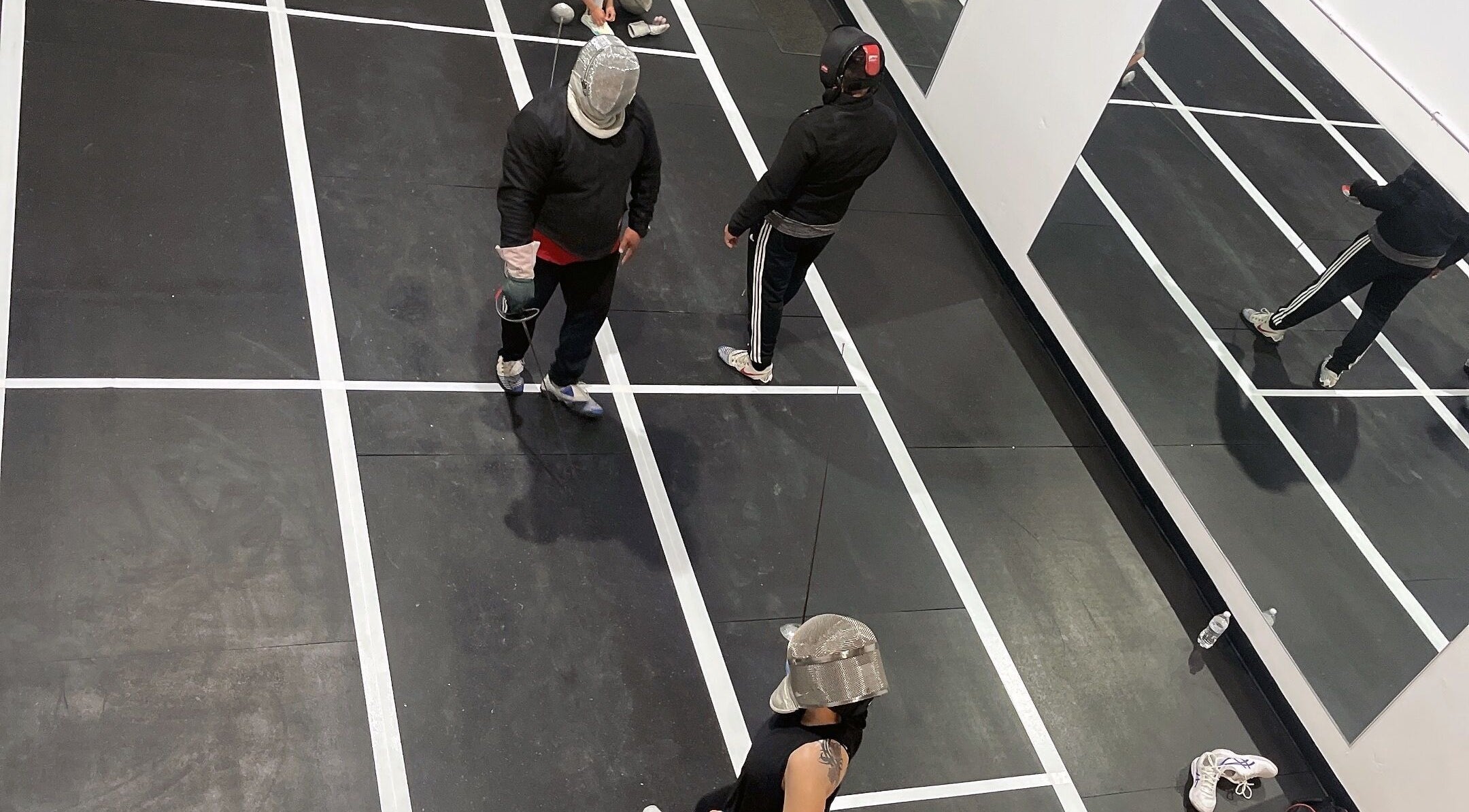 Fencers in action at Fence MI Fencing Academy, Las Vegas, Nevada, US, featuring mirrored walls and marked floors.