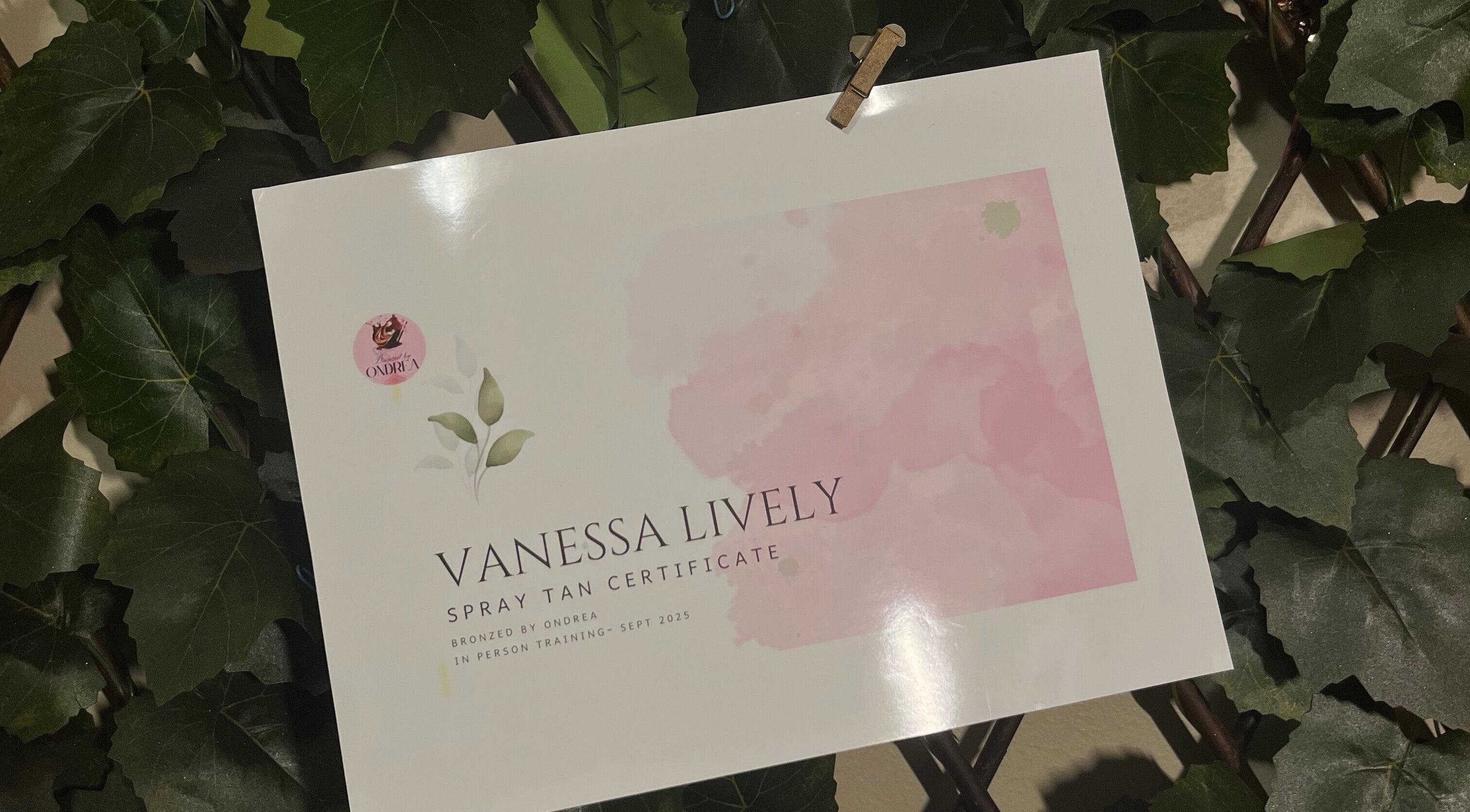 Vanessa Lively spray tan certificate at Nessknowsglow, Mossley, Ontario, CA, displayed among green leaves.