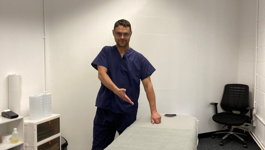 MassaAge therapist gesturing to a massage table in Manchester, England, GB for a relaxing session.