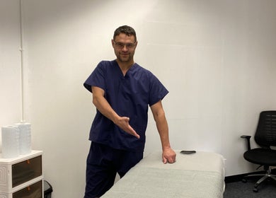 MassaAge therapist gesturing to a massage table in Manchester, England, GB for a relaxing session.