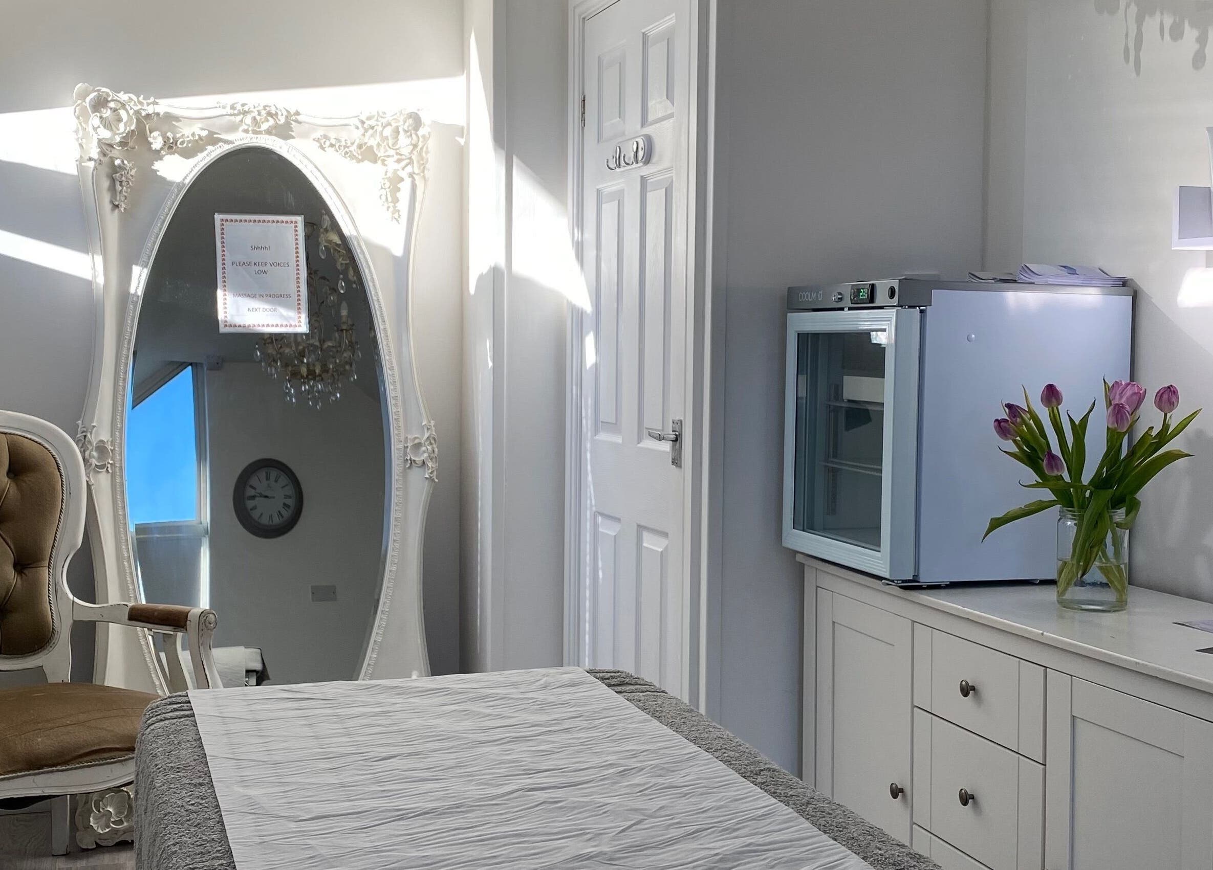 Elegant treatment room at Raha Aesthetics, Cardiff, Wales GB with vintage chair, ornate mirror, and fresh flowers.