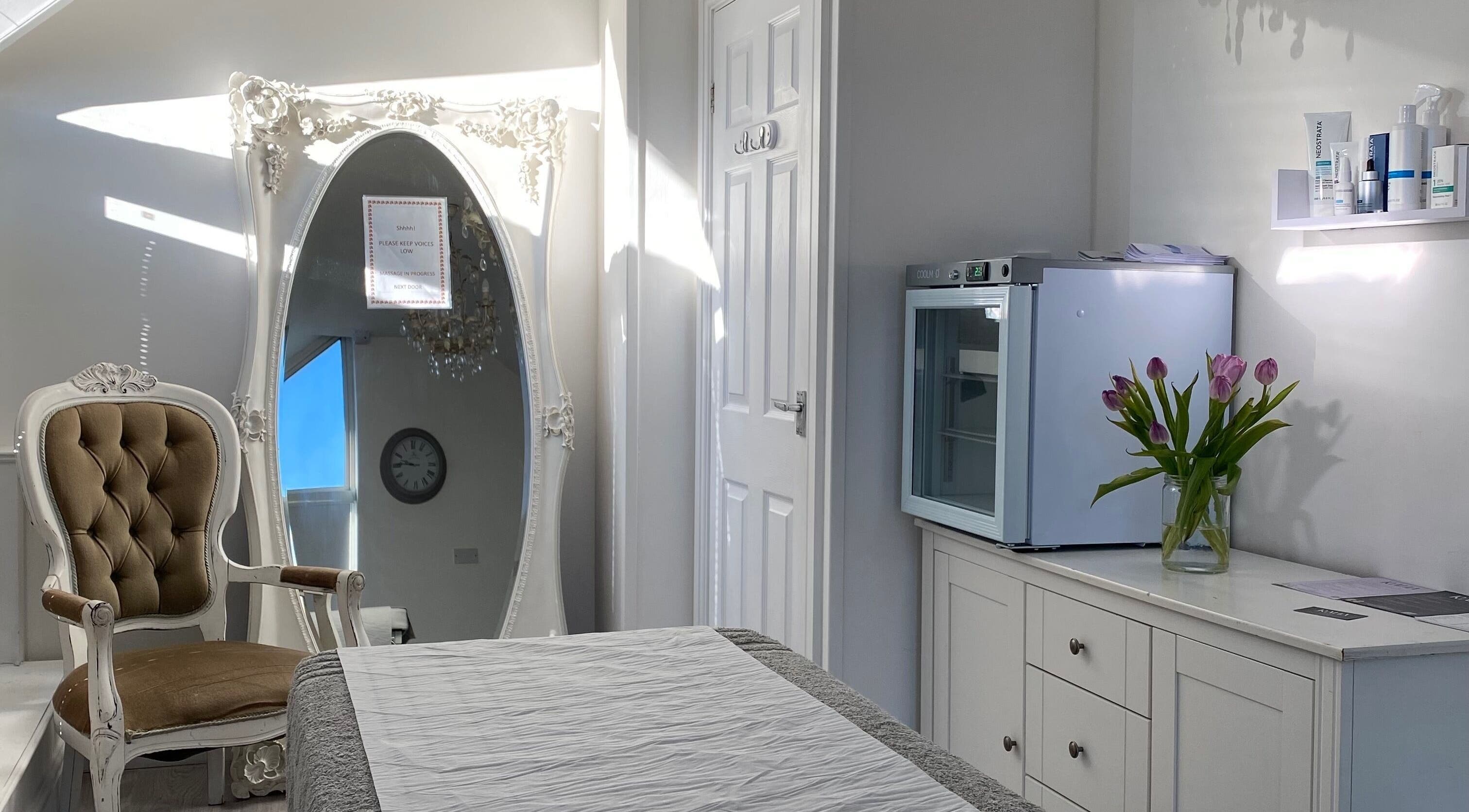 Elegant treatment room at Raha Aesthetics, Cardiff, Wales GB with vintage chair, ornate mirror, and fresh flowers.