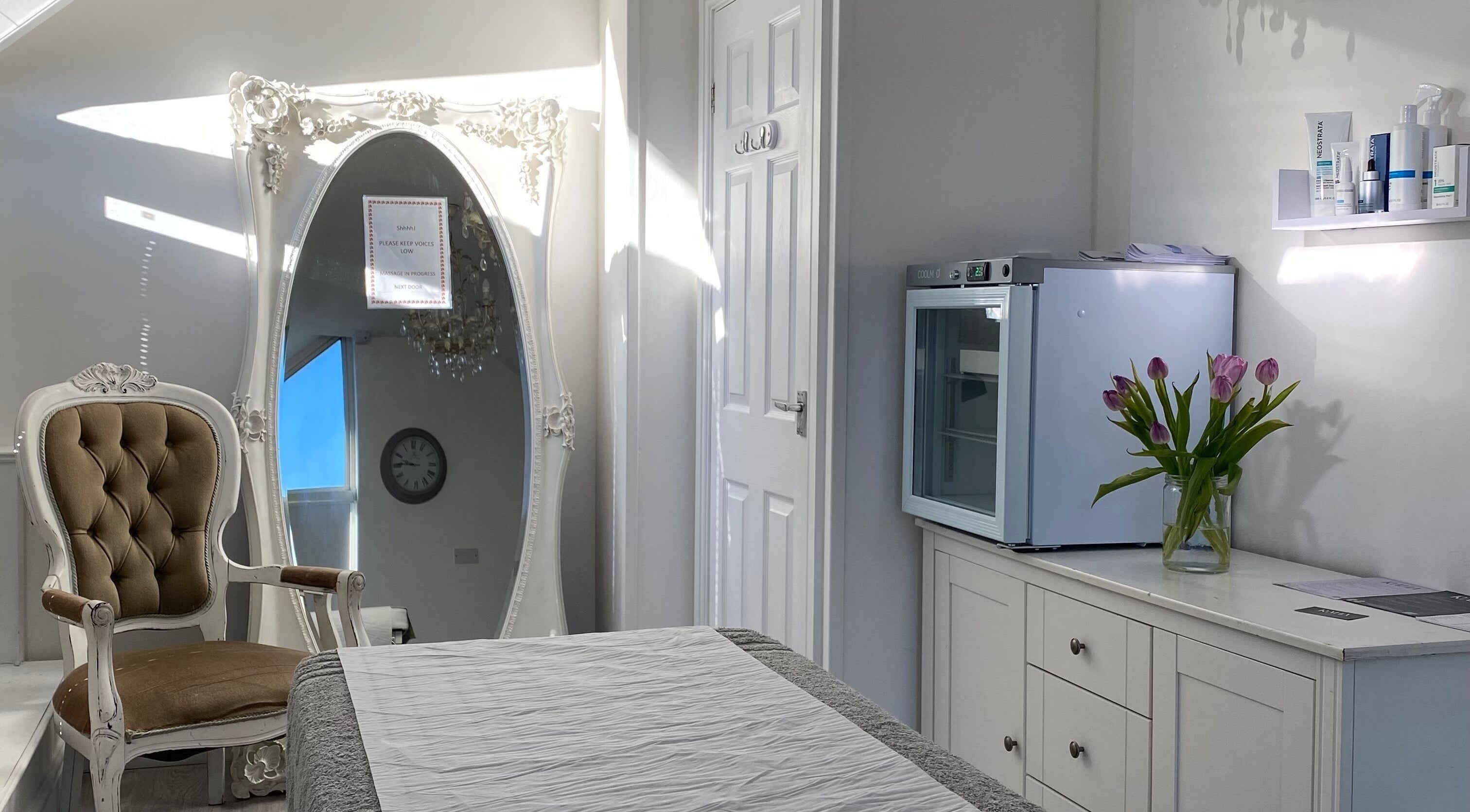 Elegant treatment room at Raha Aesthetics, Cardiff, Wales GB with vintage chair, ornate mirror, and fresh flowers.