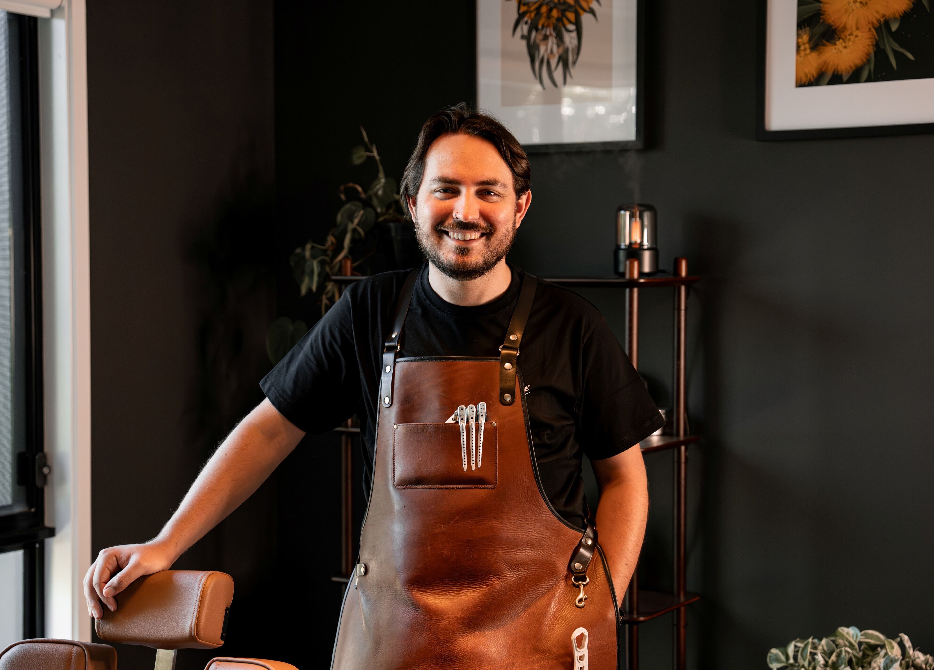 Smiling barber in apron at Caleb Sweeney Barber, Nirimba, Queensland, AU, ready to provide excellent service.