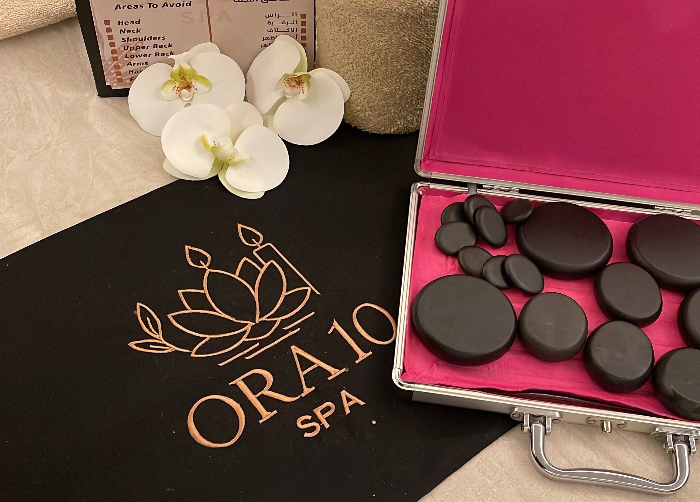 ORA10 SPA - Home Service in Riyadh offers a luxurious hot stone massage set with orchids for relaxation.