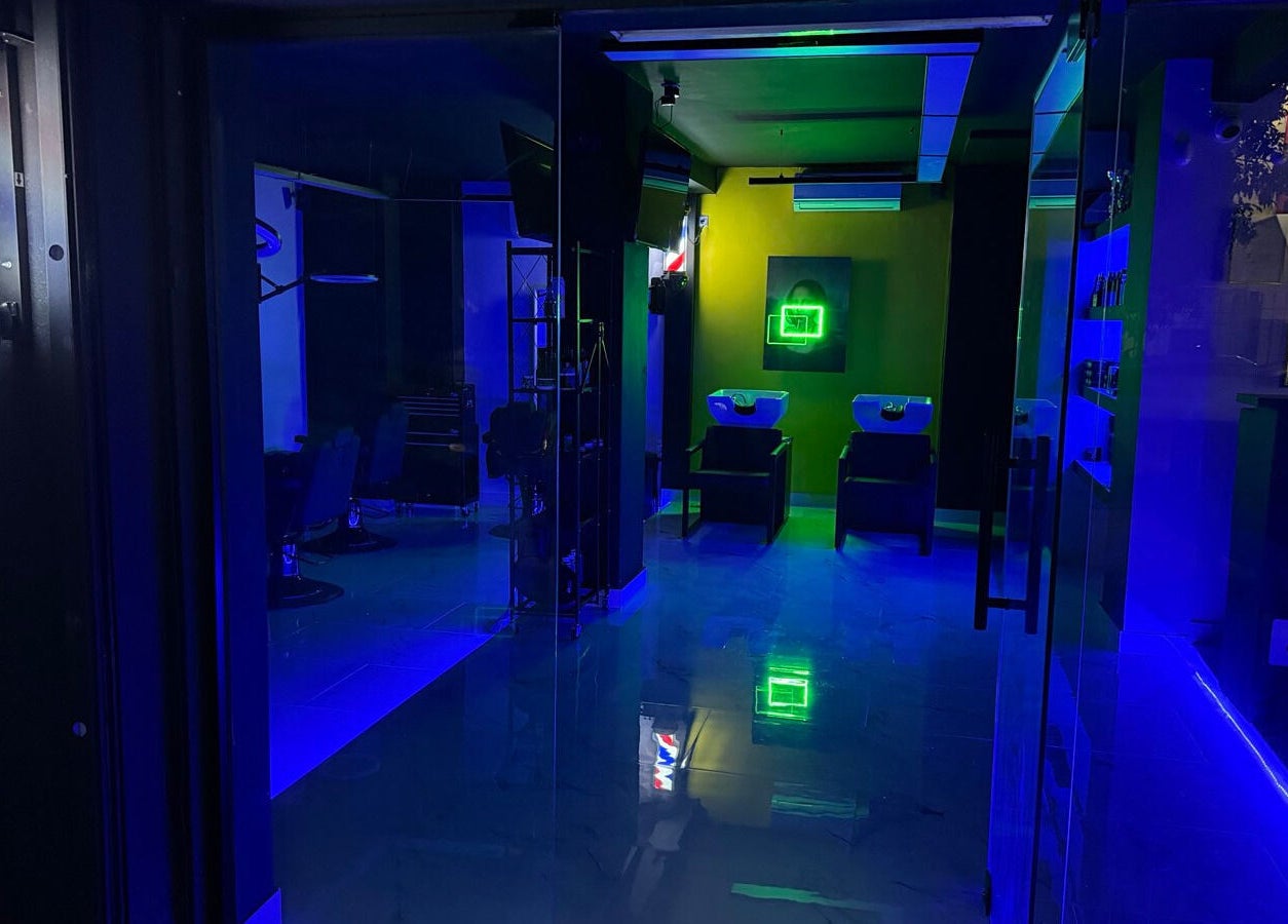 Εσωτερικό του Anestis Barber με μπλε φωτισμό, Agia Varvara, GR, δείχνει καθίσματα και νιπτήρες.