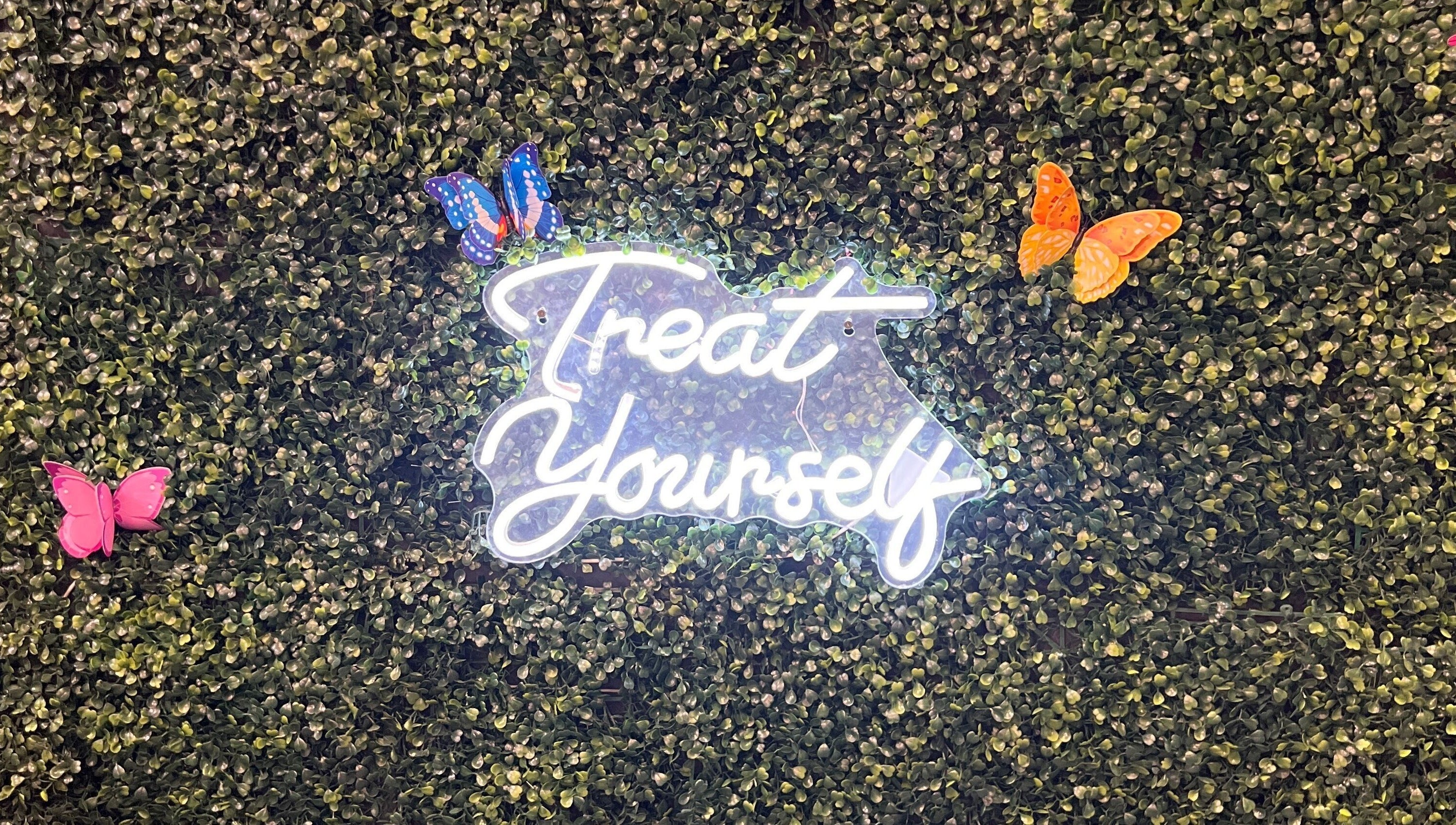 Neon 'Treat Yourself' sign surrounded by butterflies at Nicole Rose Luxe, Duluth, Georgia, US.