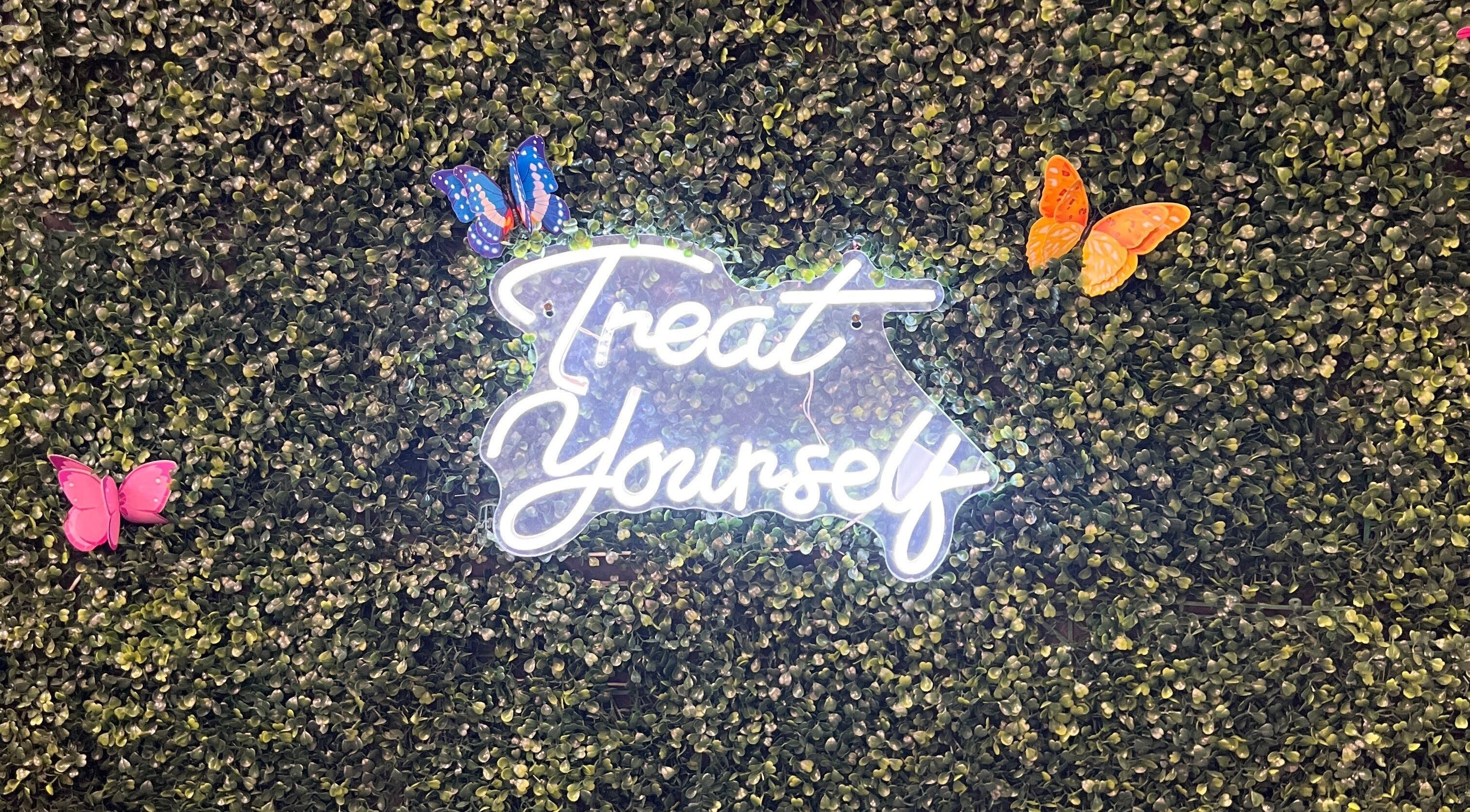 Neon 'Treat Yourself' sign surrounded by butterflies at Nicole Rose Luxe, Duluth, Georgia, US.