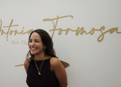 Smiling therapist at Antonia Formosa Skin Therapist, St Julian's, MT with elegant signage background.