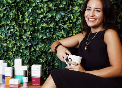 Antonia Formosa Skin Therapist in St Julian's, MT, smiling with skincare products and lush greenery.