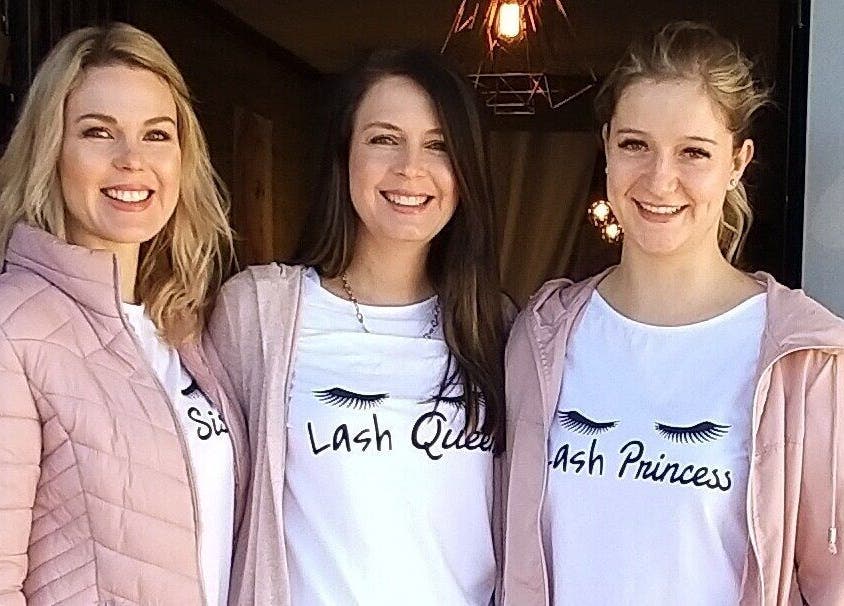 Three smiling staff members outside The Lashery George in George, Western Cape, ZA, wearing branded t-shirts.