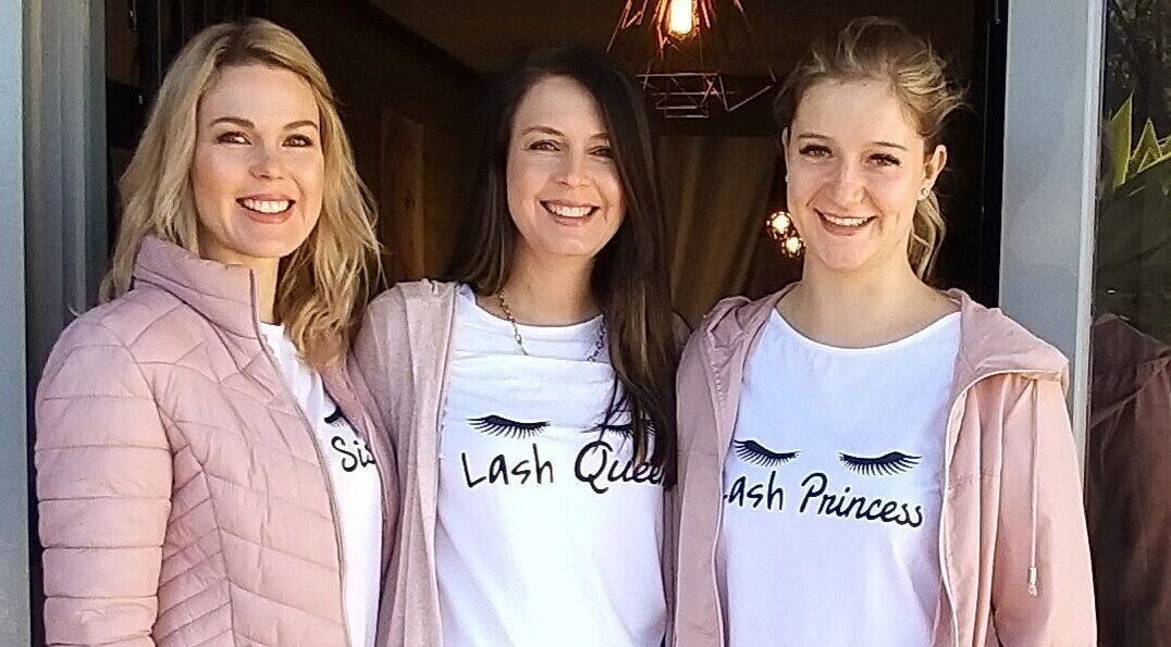 Three smiling staff members outside The Lashery George in George, Western Cape, ZA, wearing branded t-shirts.