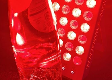 Lichttherapie bij TOAM in Dilsen-stokkem, Vlaanderen, BE met een felrode LED-paneel en waterfles.