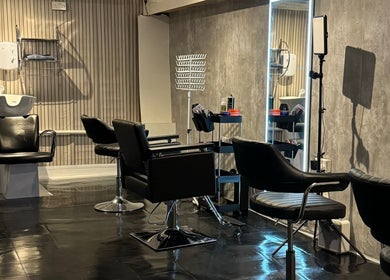 Modern hair salon interior at Hairslayedbydee, Manchester, England, GB with sleek black styling chairs.