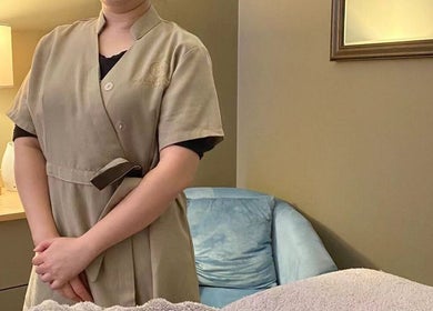 Therapist at Orenda Day Spa in Hobart, Tasmania, AU, standing beside a cozy massage table in a peaceful room.