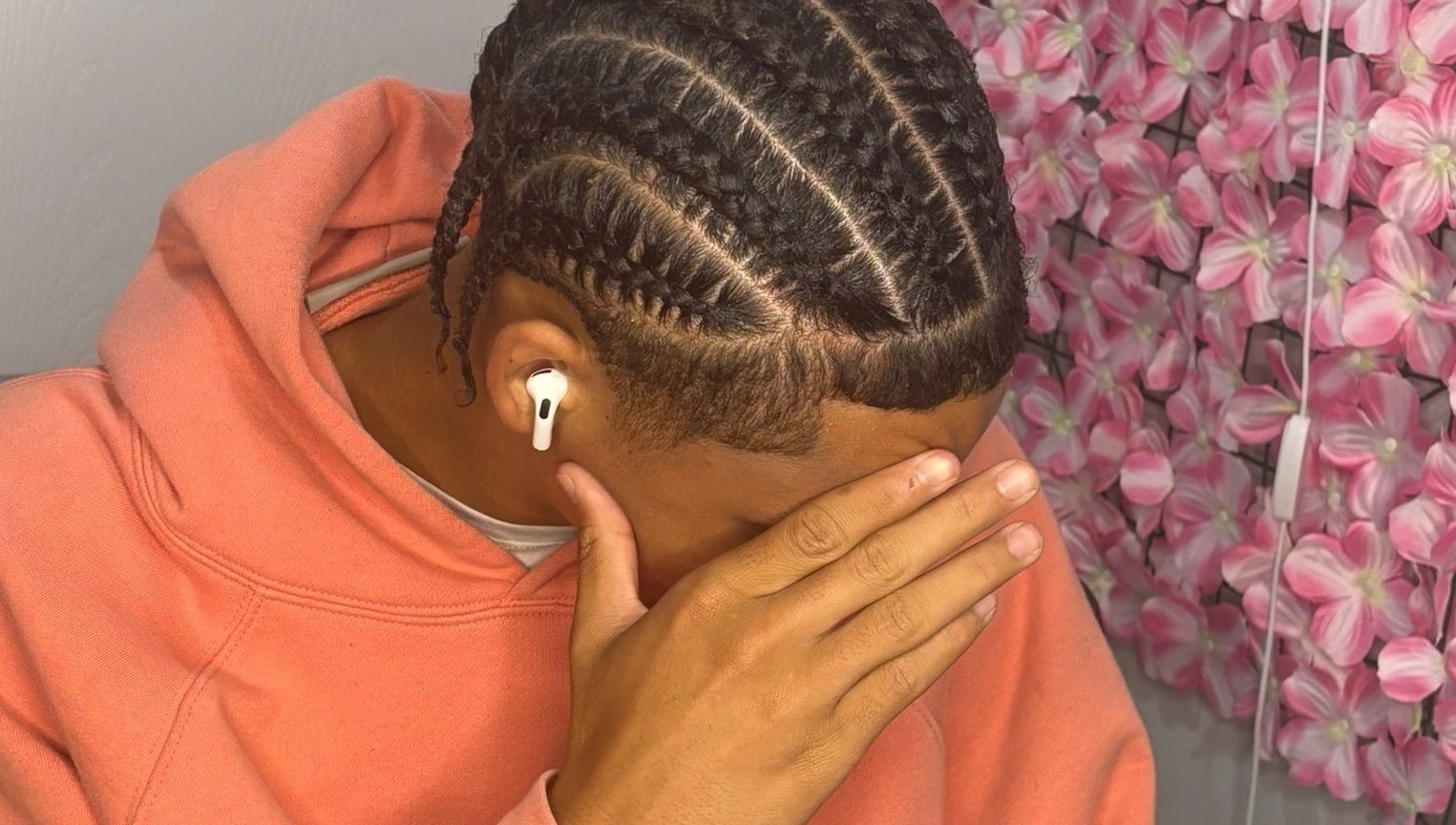 Intricate braids at Hair By Nhia, Brampton, Ontario, CA, enhance a stylish look against a pink floral wall.