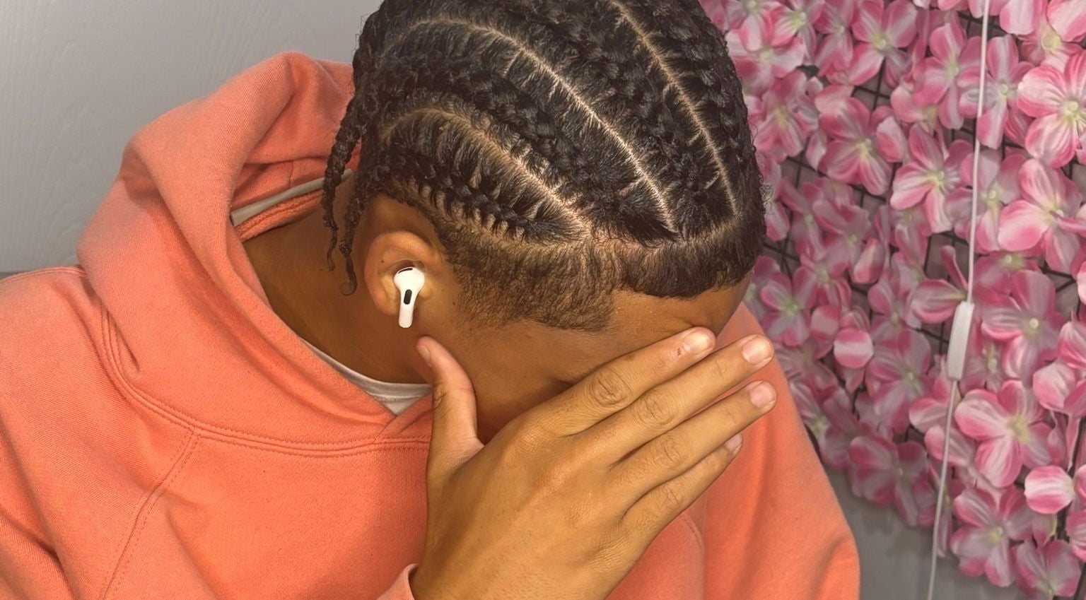 Intricate braids at Hair By Nhia, Brampton, Ontario, CA, enhance a stylish look against a pink floral wall.