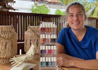 Nagellakdisplay en medewerker bij El Fuego Pedicure en Manicure in Willemstad, CW. Palmbomen op achtergrond.