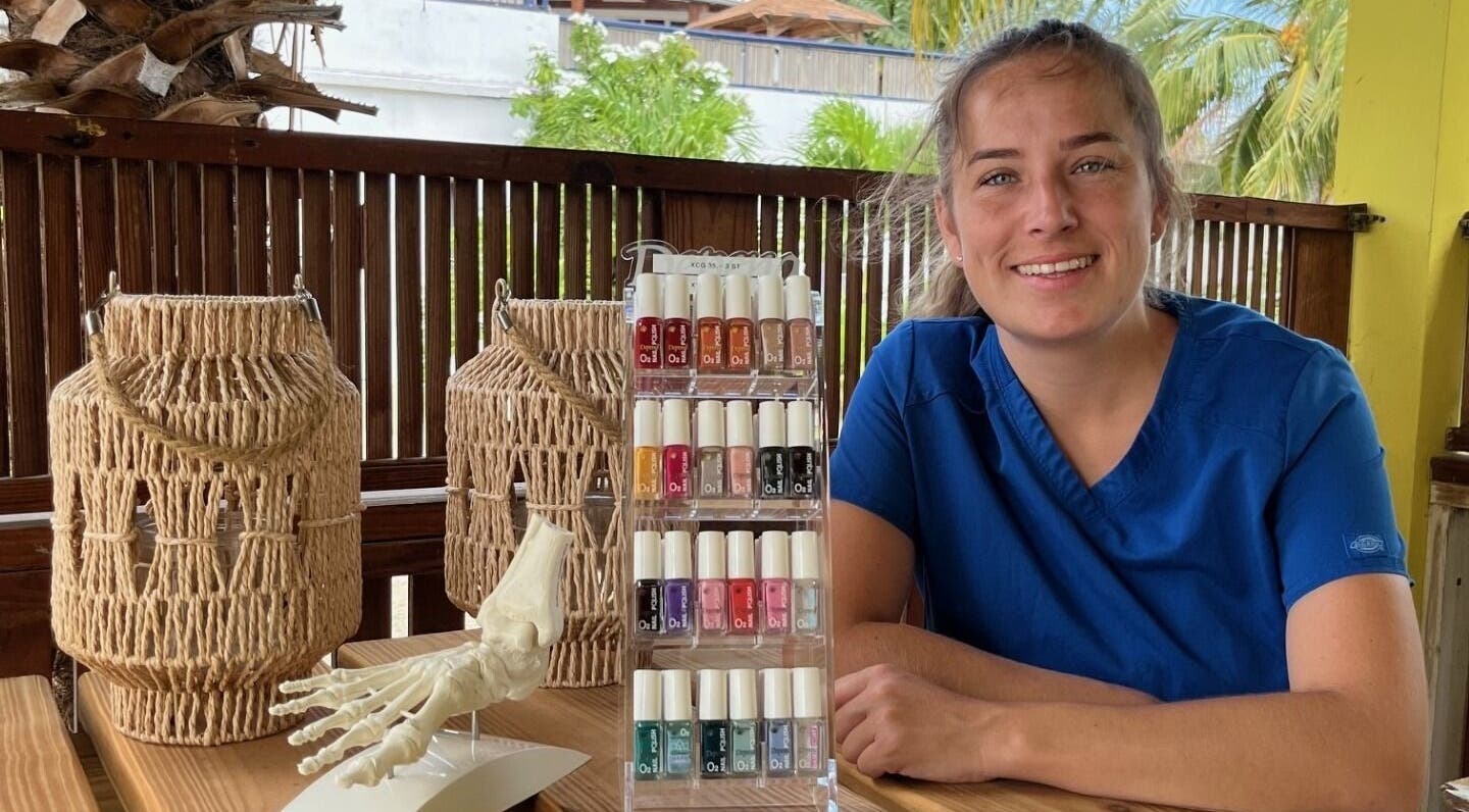 Nagellakdisplay en medewerker bij El Fuego Pedicure en Manicure in Willemstad, CW. Palmbomen op achtergrond.