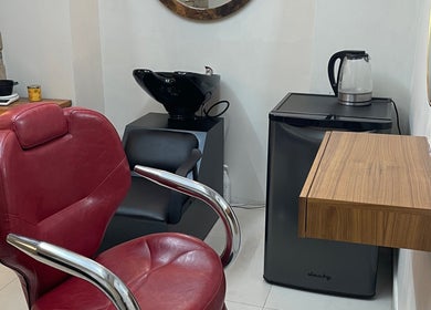 Silla de salón roja en N&H Vital Hair, Chihuahua, Chihuahua, MX, junto a un lavamanos y una pequeña nevera.