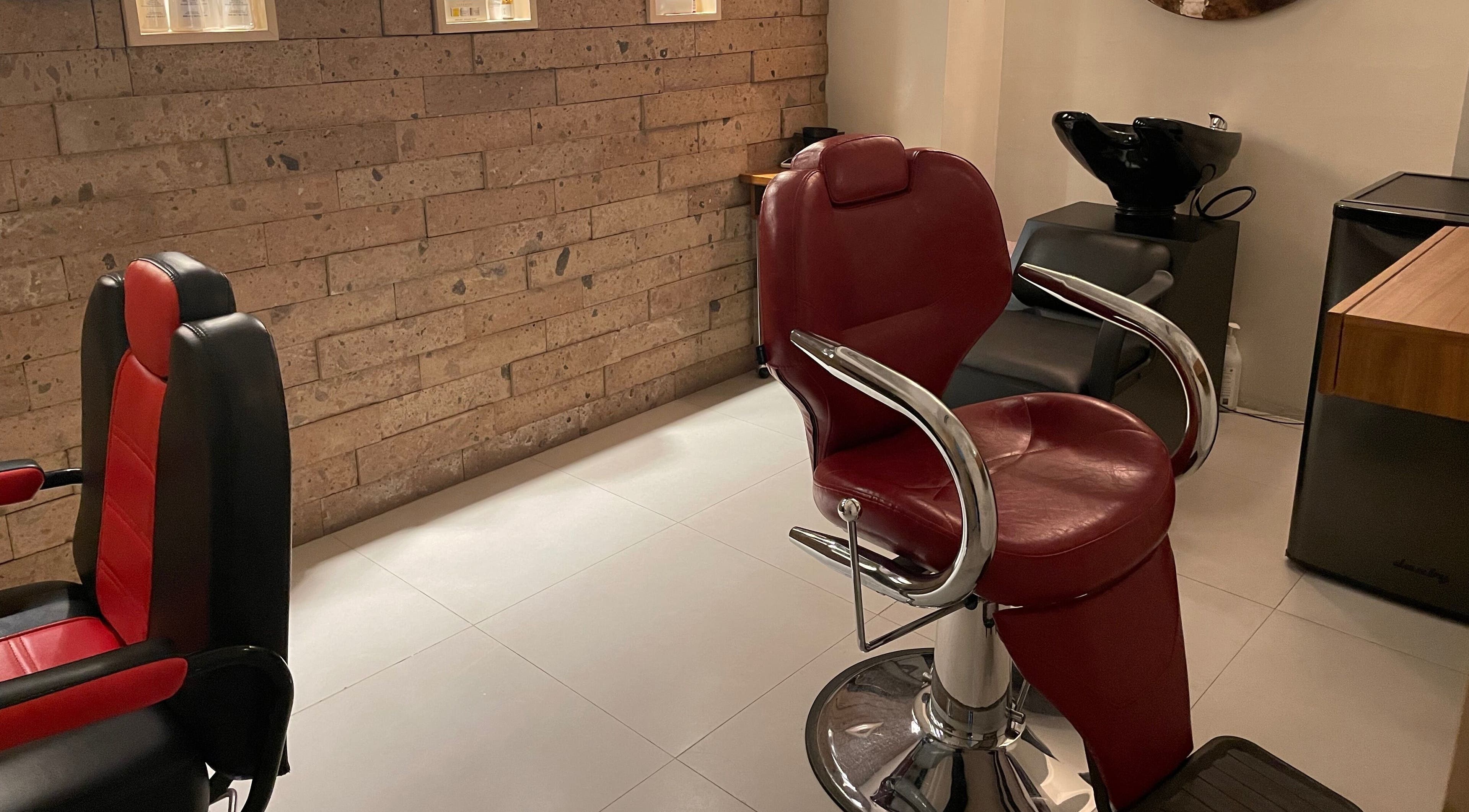 Interior del salón N&H Vital Hair en Chihuahua, MX, con sillón rojo y paredes de ladrillo.