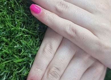 Bright pink manicure on hands at BeYouBeauty, Larne, Northern Ireland, GB, against green grass background.