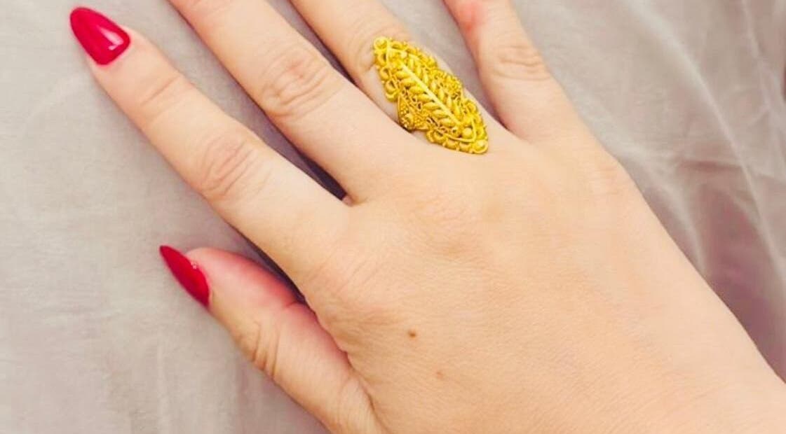 Elegantly manicured hand with red nails and gold ring at Glow Up, Cape Town, Western Cape, ZA.