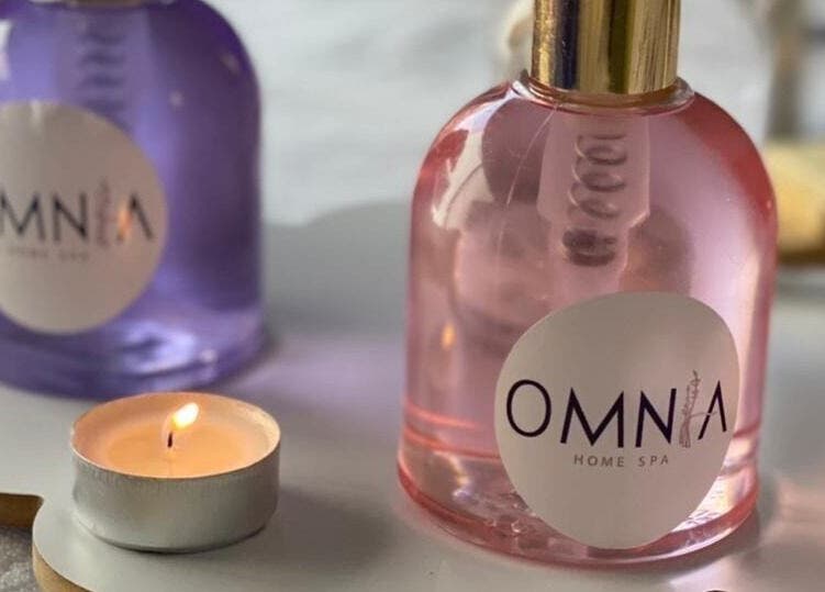 زجاجة عطر وشمعة مشتعلة بجانبها في Omnia Spa Home Service | Riyadh، الرياض، منطقة الرياض، السعودية.