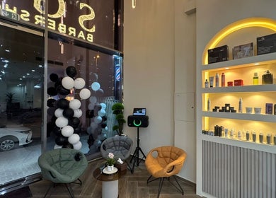 Welcoming interior of SGC Barbershop in Dubai, Dubai, AE, featuring comfy chairs and a lit product shelf.
