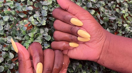 Stylish yellow manicure on dark skin at PS Nail Bar, Randburg, Gauteng, ZA, accentuated by green foliage.