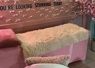 Ροζ μοντέρνος χώρος θεραπείας στο Dolly Beauty House, Θεσσαλονίκη, GR, με καναπέ και διακοσμητικά λουλούδια.