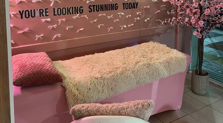 Ροζ μοντέρνος χώρος θεραπείας στο Dolly Beauty House, Θεσσαλονίκη, GR, με καναπέ και διακοσμητικά λουλούδια.