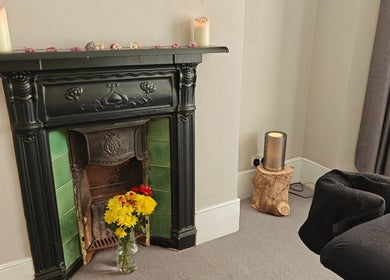 Cozy room at Awaken Holistic Healing in London, England, GB with candles and flowers on a vintage fireplace.