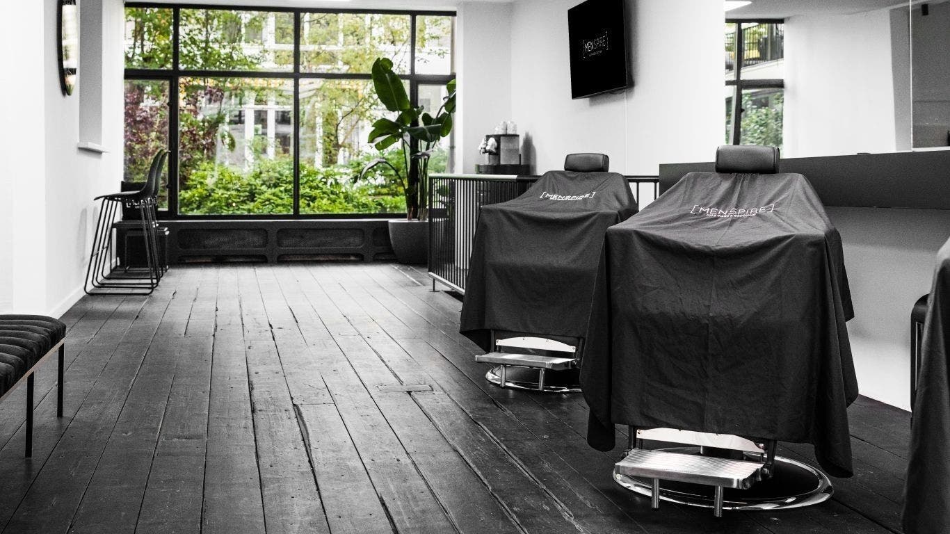 Modern barber chairs at MENSPIRE Old South, Amsterdam, Noord-Holland, NL with lush greenery outside.