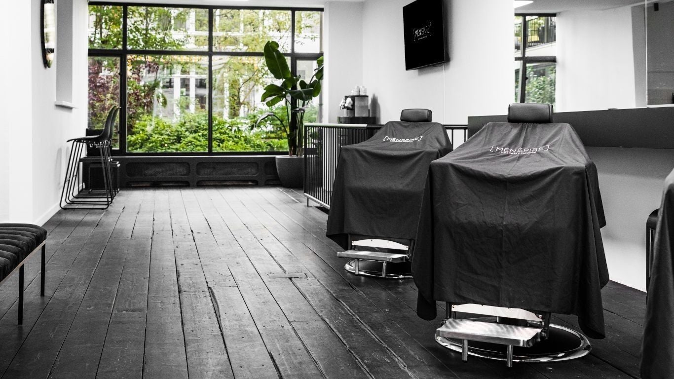 Modern barber chairs at MENSPIRE Old South, Amsterdam, Noord-Holland, NL with lush greenery outside.