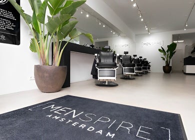 Inside MENSPIRE De Pijp in Amsterdam, Noord-Holland, NL, featuring modern barbershop chairs and lush greenery.