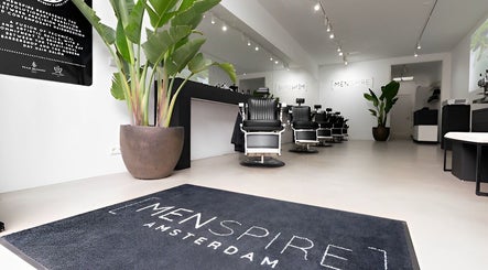 Inside MENSPIRE De Pijp in Amsterdam, Noord-Holland, NL, featuring modern barbershop chairs and lush greenery.