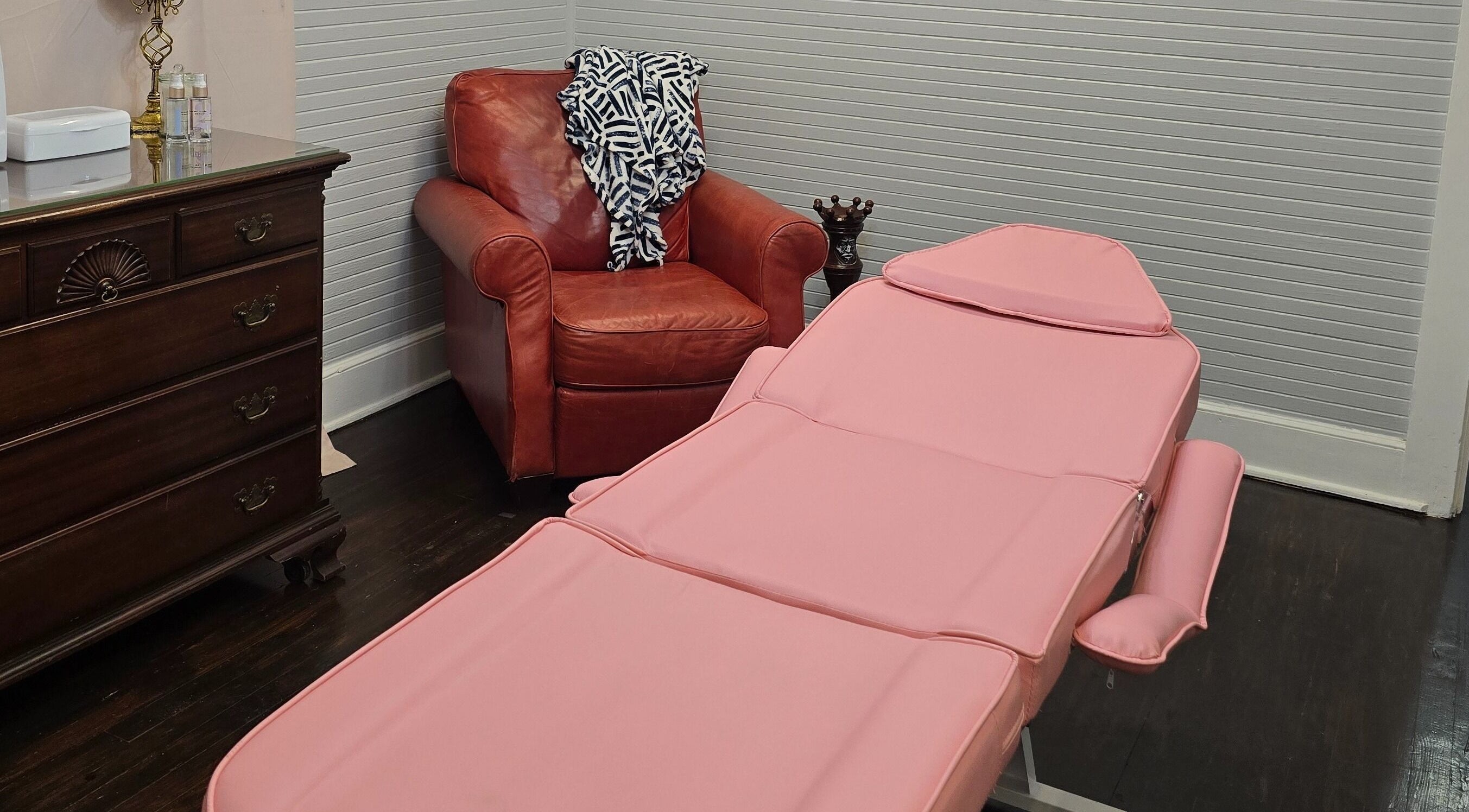 Relaxing treatment room at Worth The Rip, Blythewood, South Carolina, US, featuring pink massage bed and red chair.