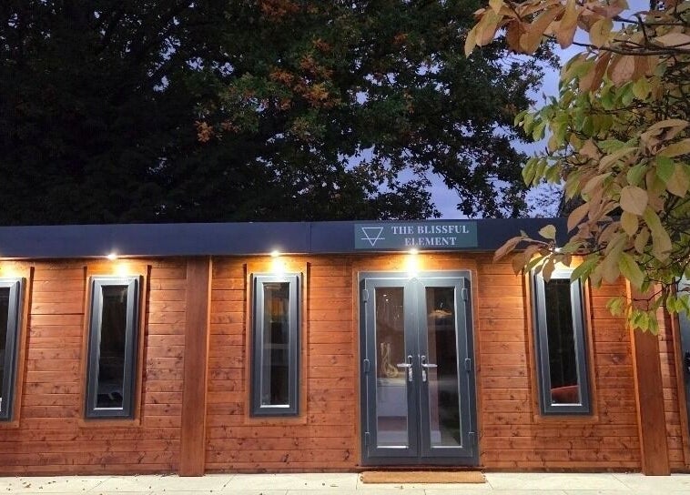 Front view of The Blissful Element in Chandler's Ford, England, GB showcasing a wooden facade and ambient lighting.
