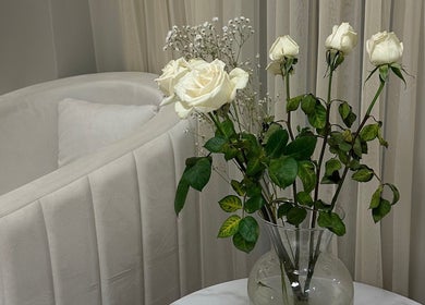 White roses in a vase beside a plush chair, enhancing 92 Lakeshore Road East in Mississauga, Ontario, CA.