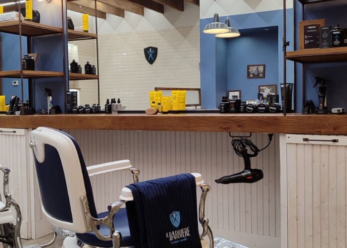 Interno moderno di Il Barbiere Cremona, situato a Cremona, Lombardia, IT con poltrone stilistiche e prodotti di bellezza.